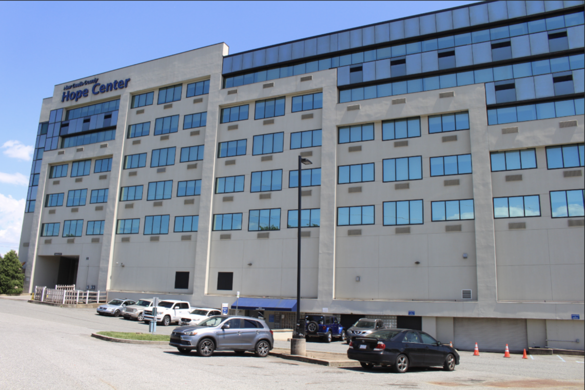 A multi-story building with several cars parked in front. The sign reads "Hope Center" atop. The structure has large windows and a beige facade.